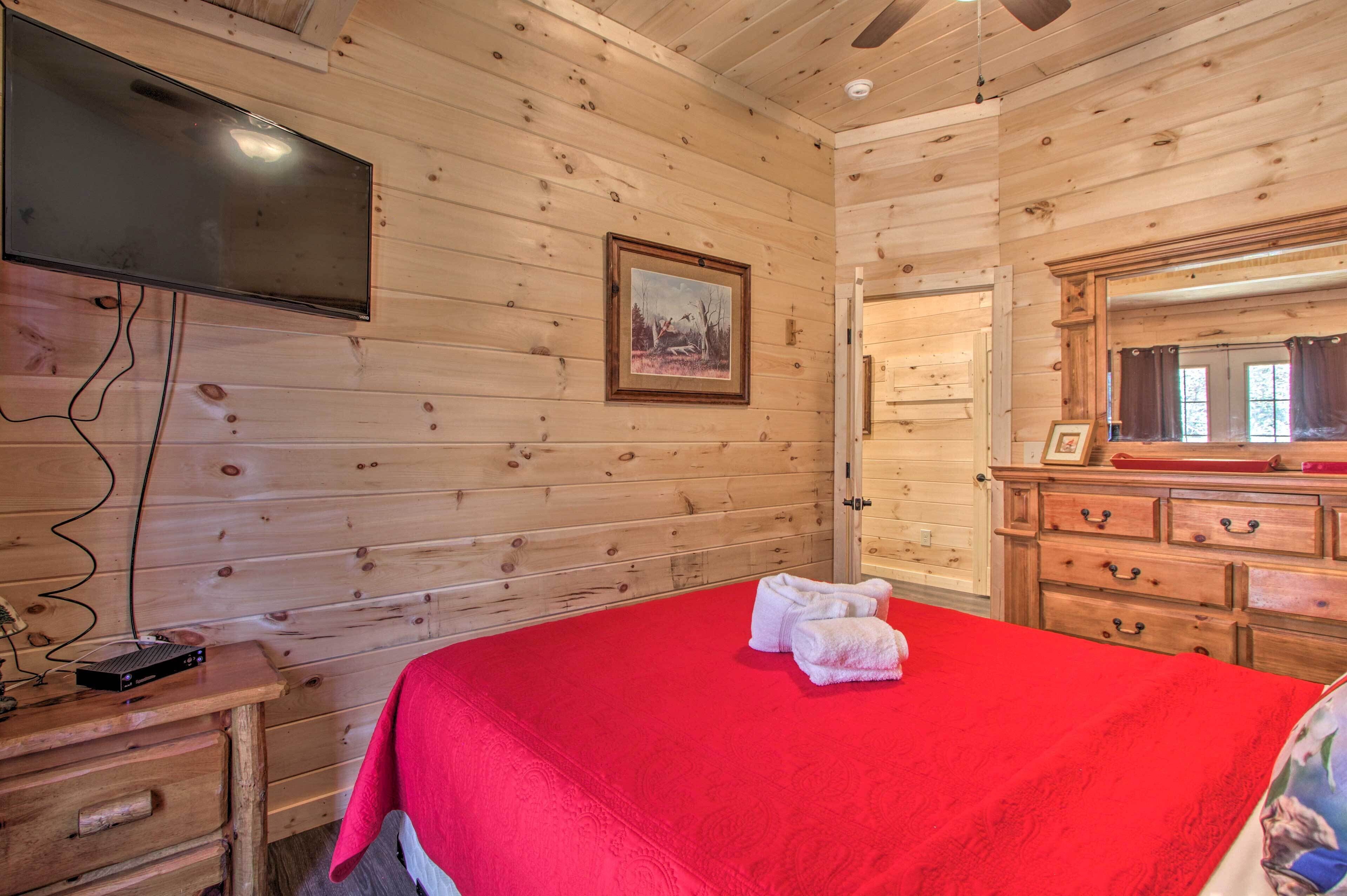 A wooden cabin room with a bed, a TV, a dresser, and a framed picture on the wall.
