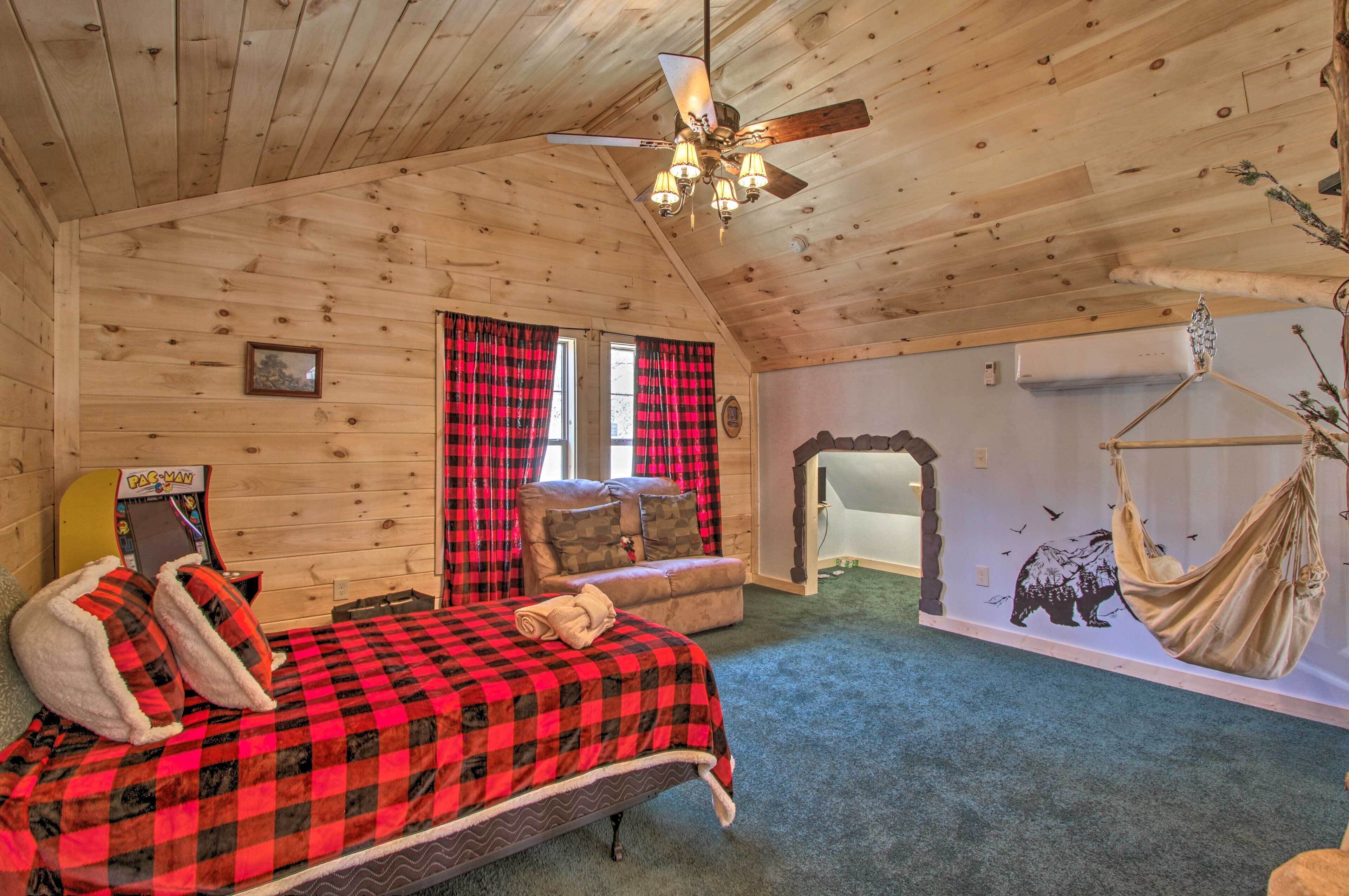 A cozy cabin room with a bed, a ceiling fan, a hammock, and a wall-mounted air conditioning unit.