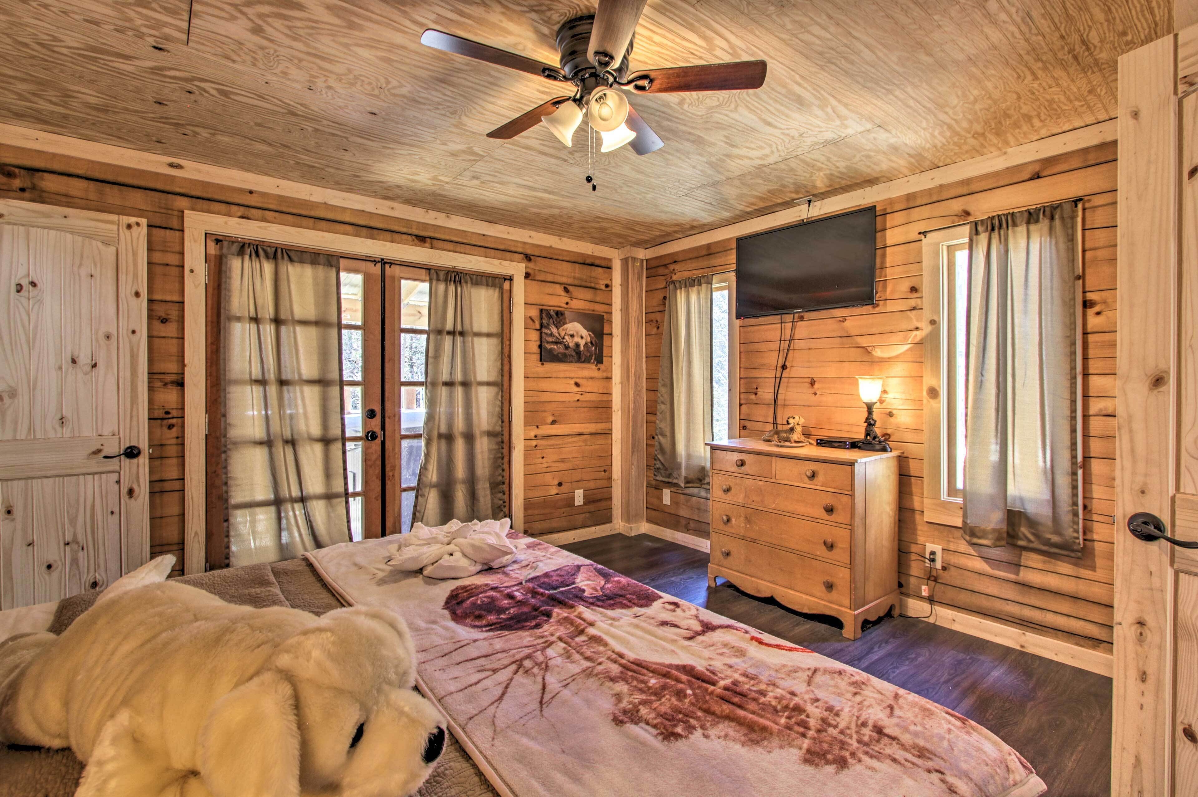 A wooden cabin bedroom with a bed, a dresser, a ceiling fan, and a TV.