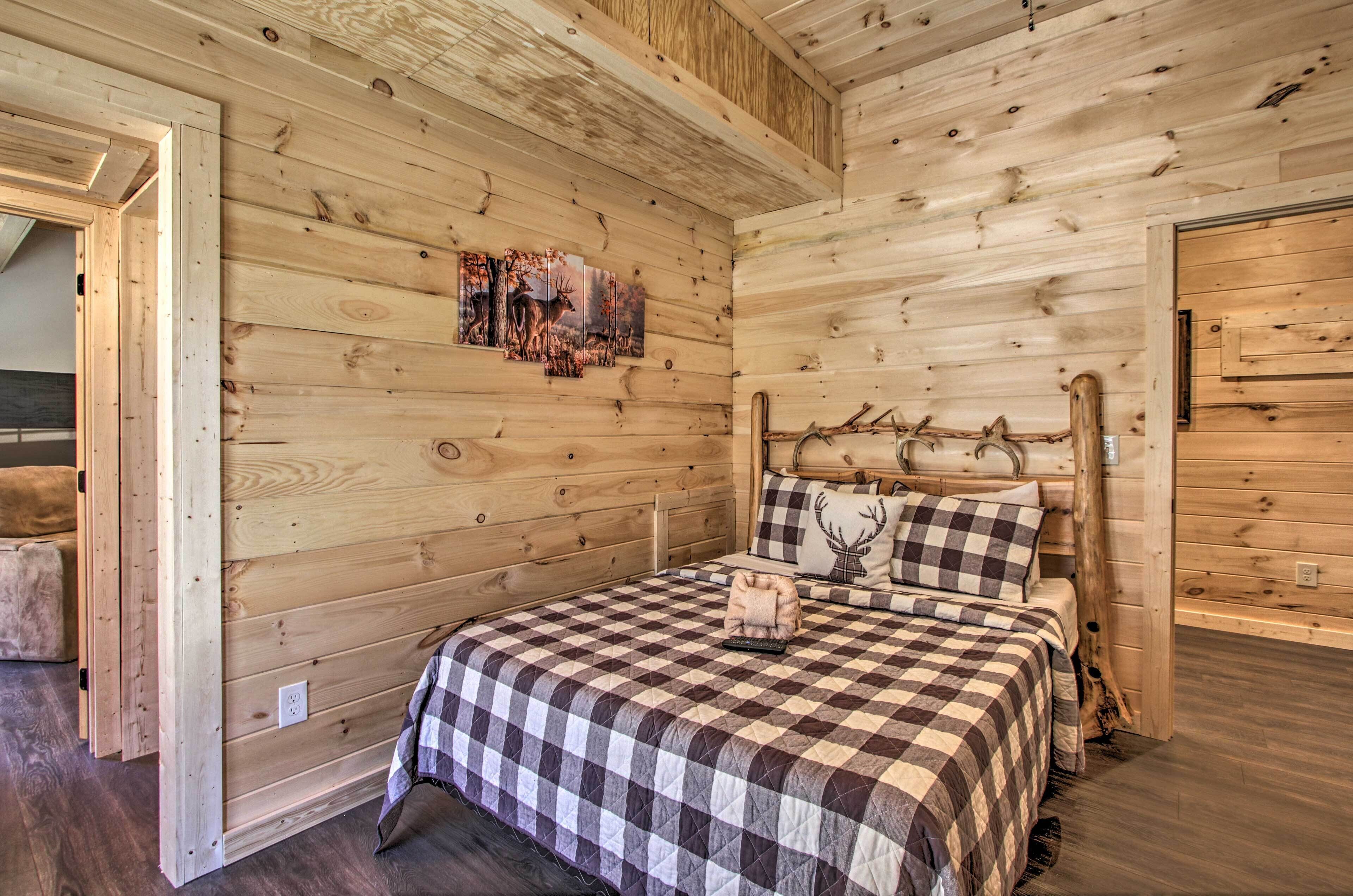 Un dormitorio de cabaña de madera con colcha a cuadros, un venado montado en la cabecera y un cuadro de ciervos en la pared.