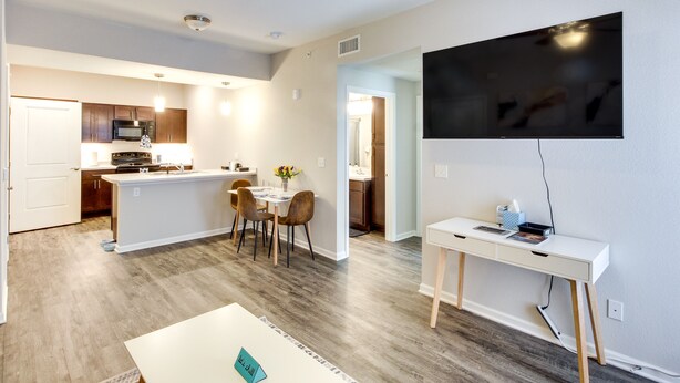 Une cuisine moderne dotée d’un îlot central, d’un coin repas avec des chaises, d’un téléviseur à écran plat fixé au mur et d’un bureau avec un ordinateur.