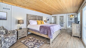 Une chambre avec un plafond en bois, un lit avec une tête de lit, une table de chevet, une commode et un canapé à motifs.