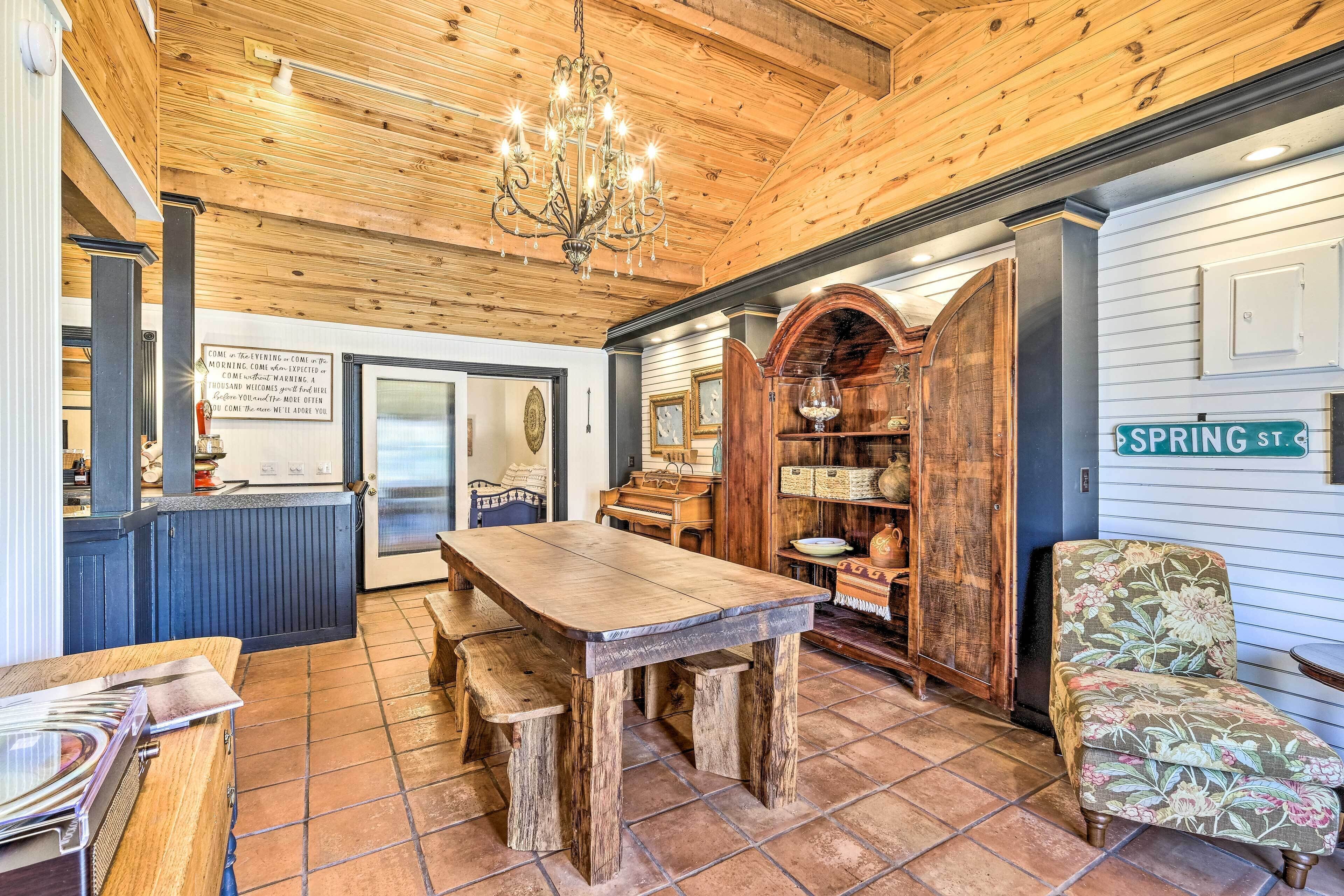 A rustic kitchen with a wooden table and bench, a chandelier, and a bookshelf.