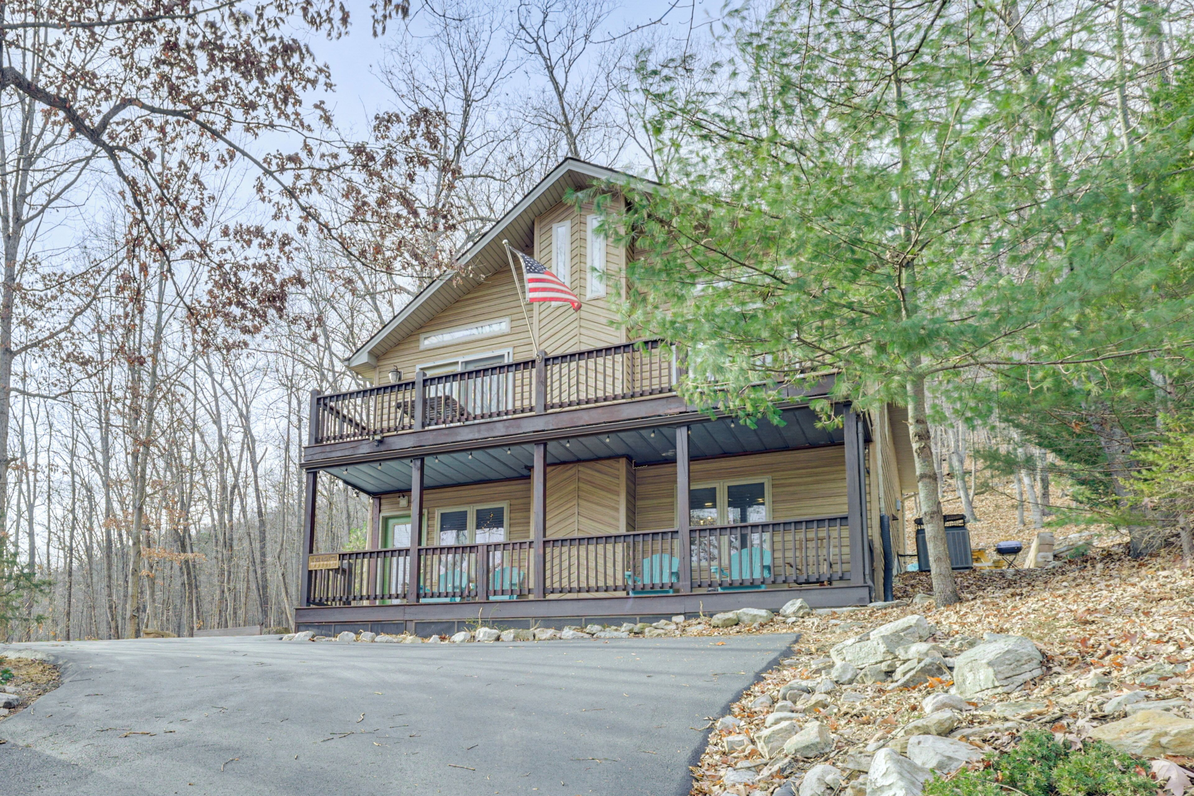 A two-story cabin with a balcony, surrounded by trees and a stone pathway.