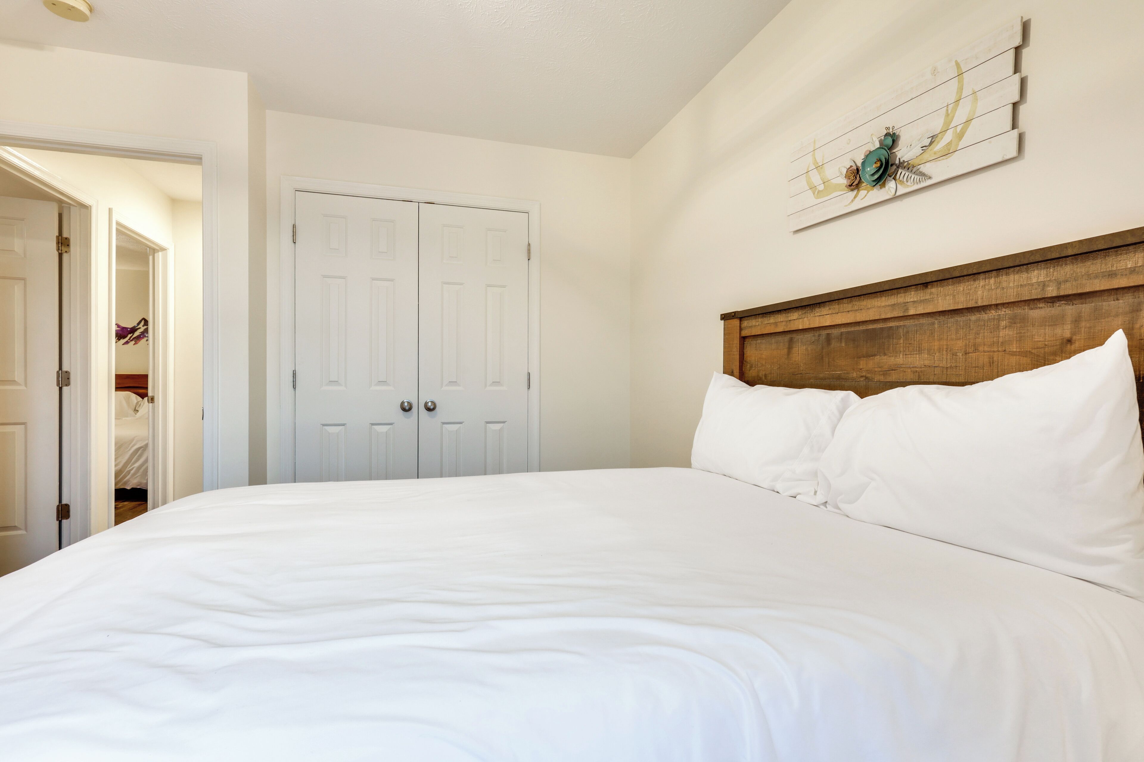 A bedroom with a large bed, white walls, a wooden headboard, and a door with a decorative wall piece above it.