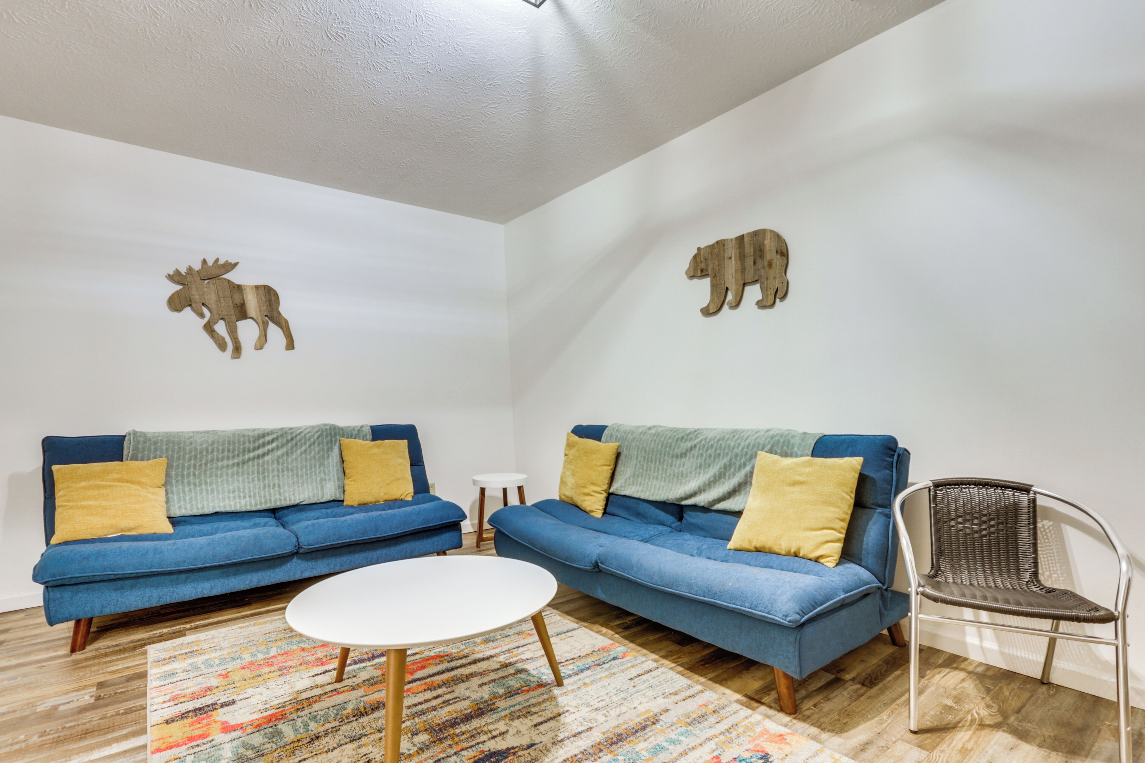Una sala de estar con dos sofás azules, una mesa de centro blanca, un tapete estampado y una silla de mimbre.