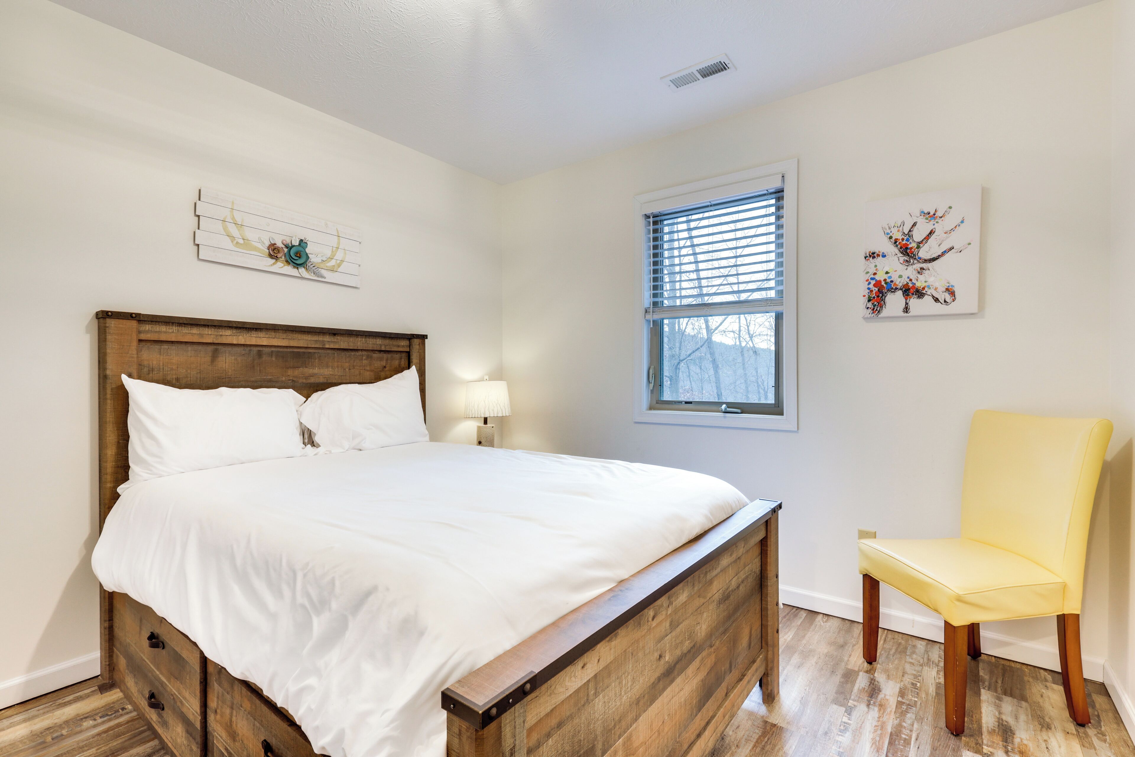 Een slaapkamer met een houten bed, een nachtkastje met lamp, een raam met zonwering en een stoel.
