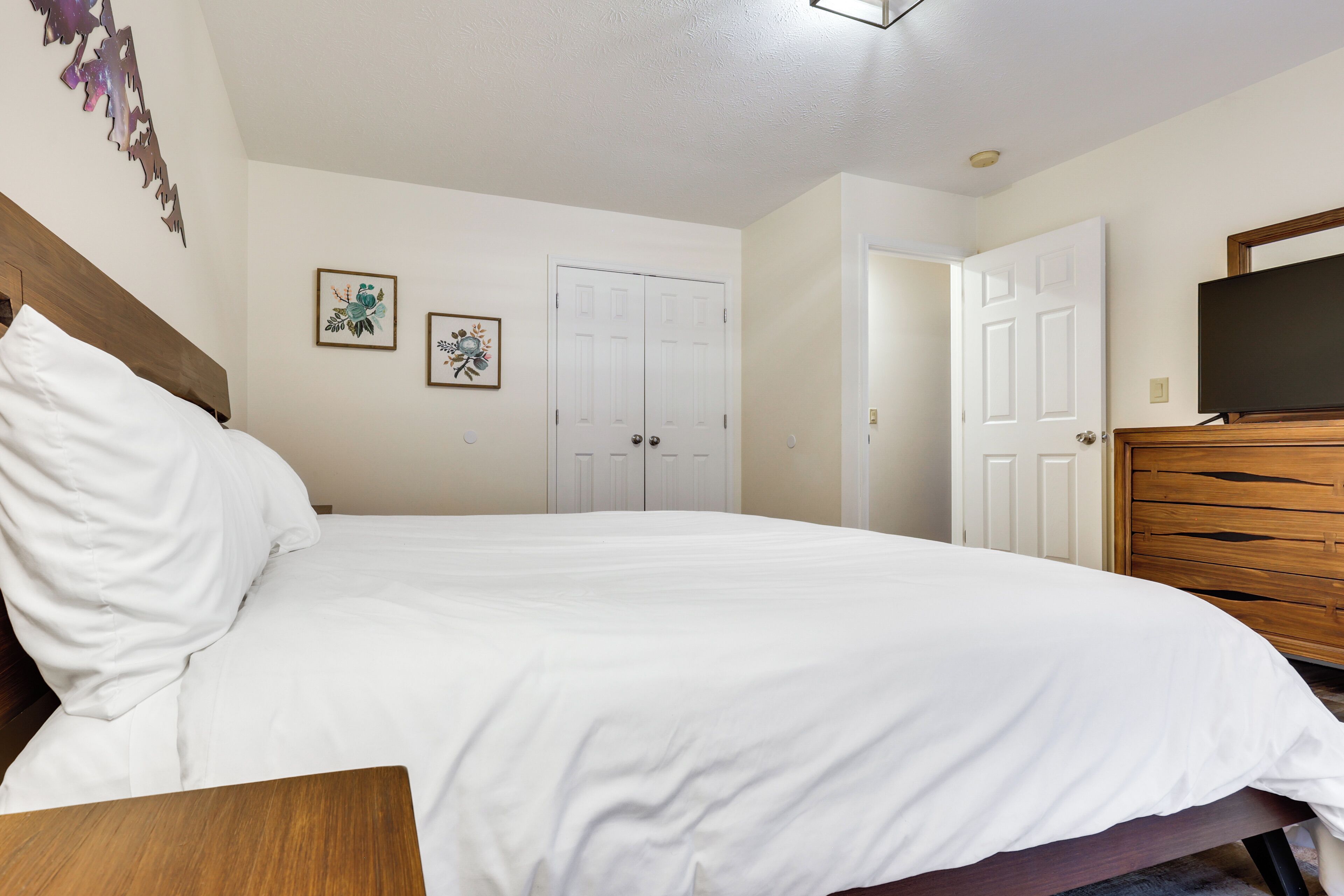 A neatly made bed in a room with a wooden headboard, a dresser, and a television mounted on the wall.