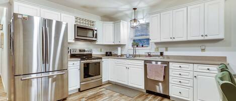 Una cocina moderna con gabinetes blancos, electrodomésticos de acero inoxidable y piso de madera.