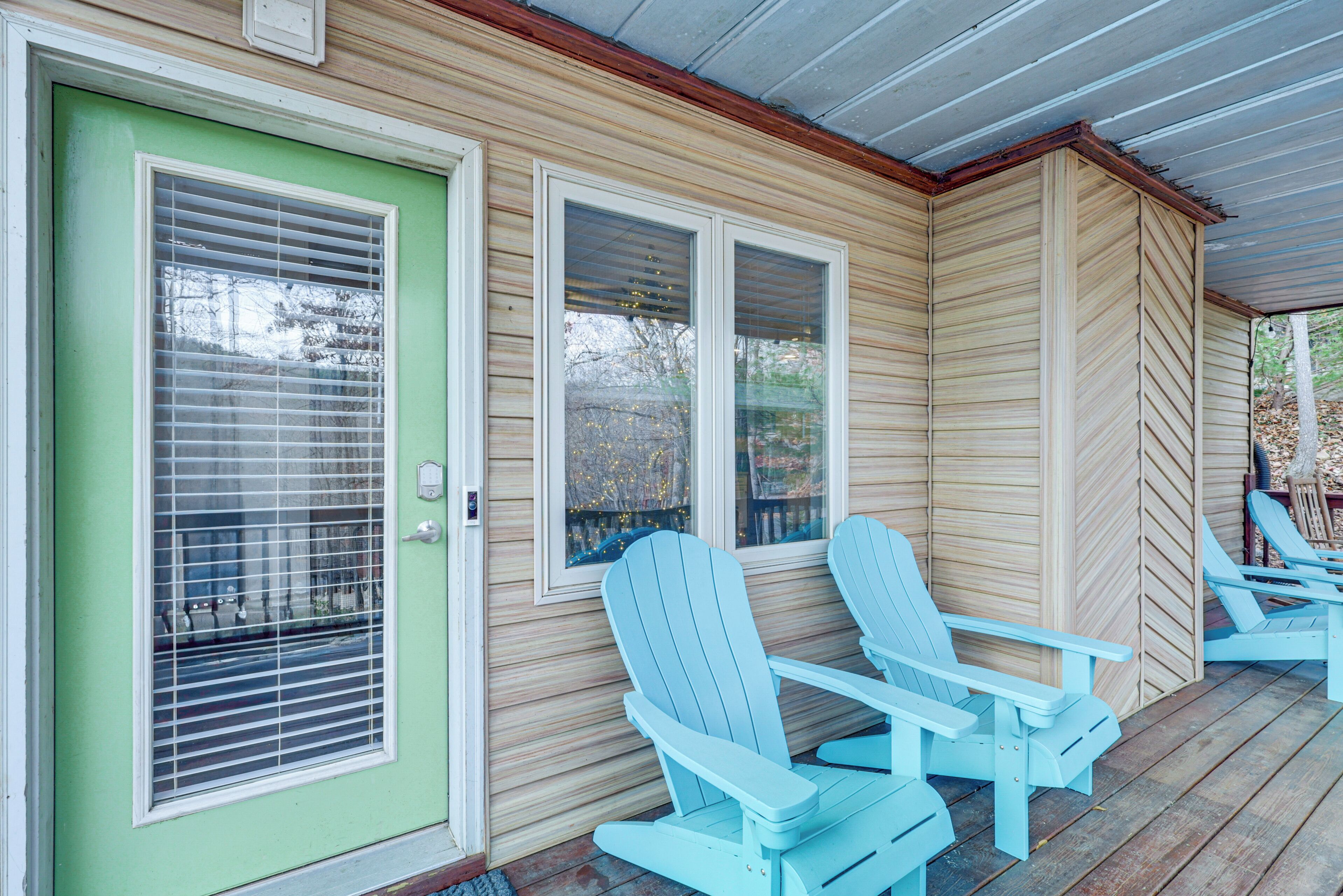 A porch with two Adirondack chairs, a green door with a window, and a wooden exterior.