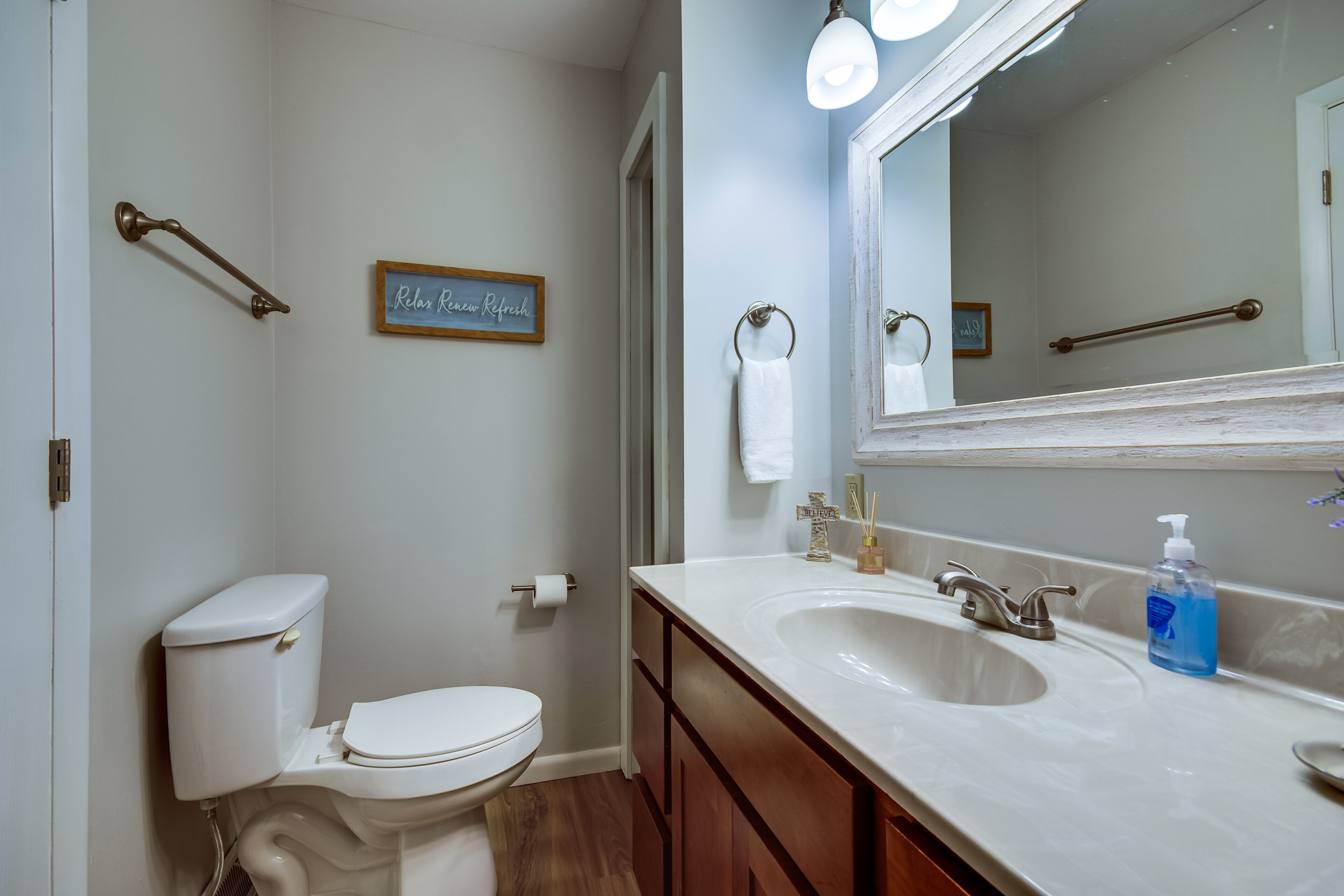 A bathroom with a toilet, sink, mirror, and a towel rack.