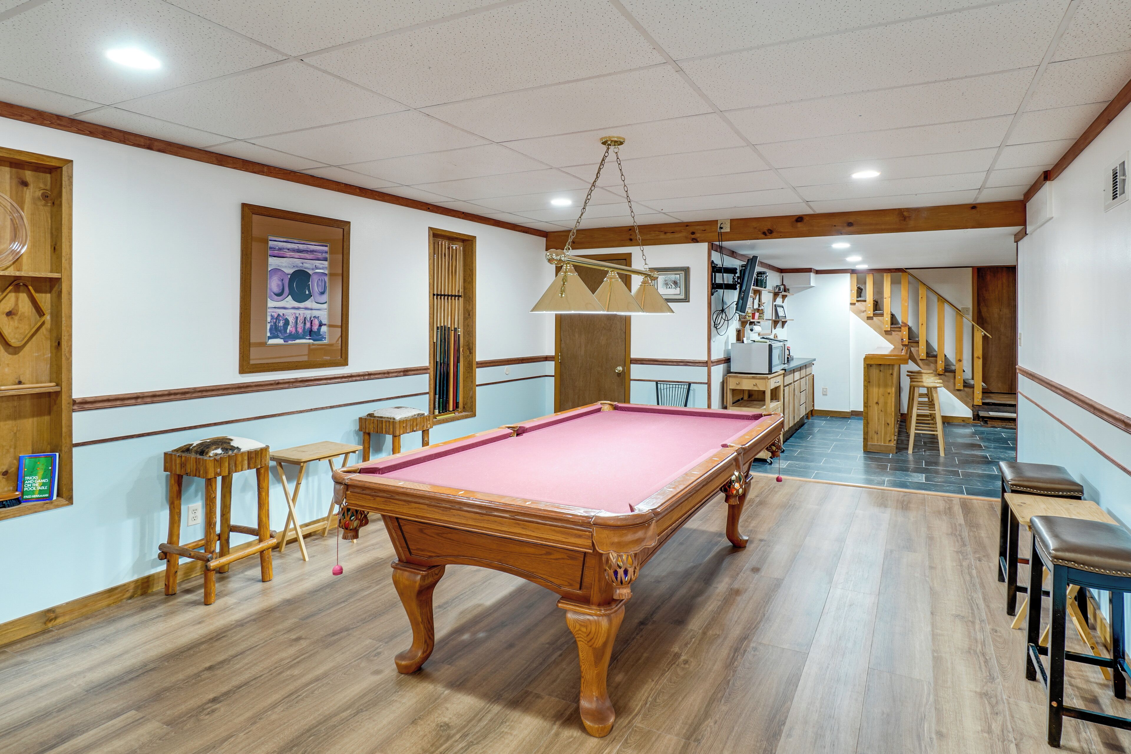 A pool table in a room with wooden flooring, a staircase, and a door leading to another area.