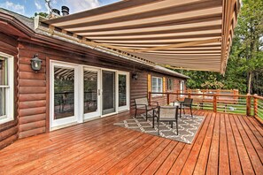 Um deck de madeira com um espaço coberto de varanda, uma mesa com cadeiras e vista para a paisagem ao redor.