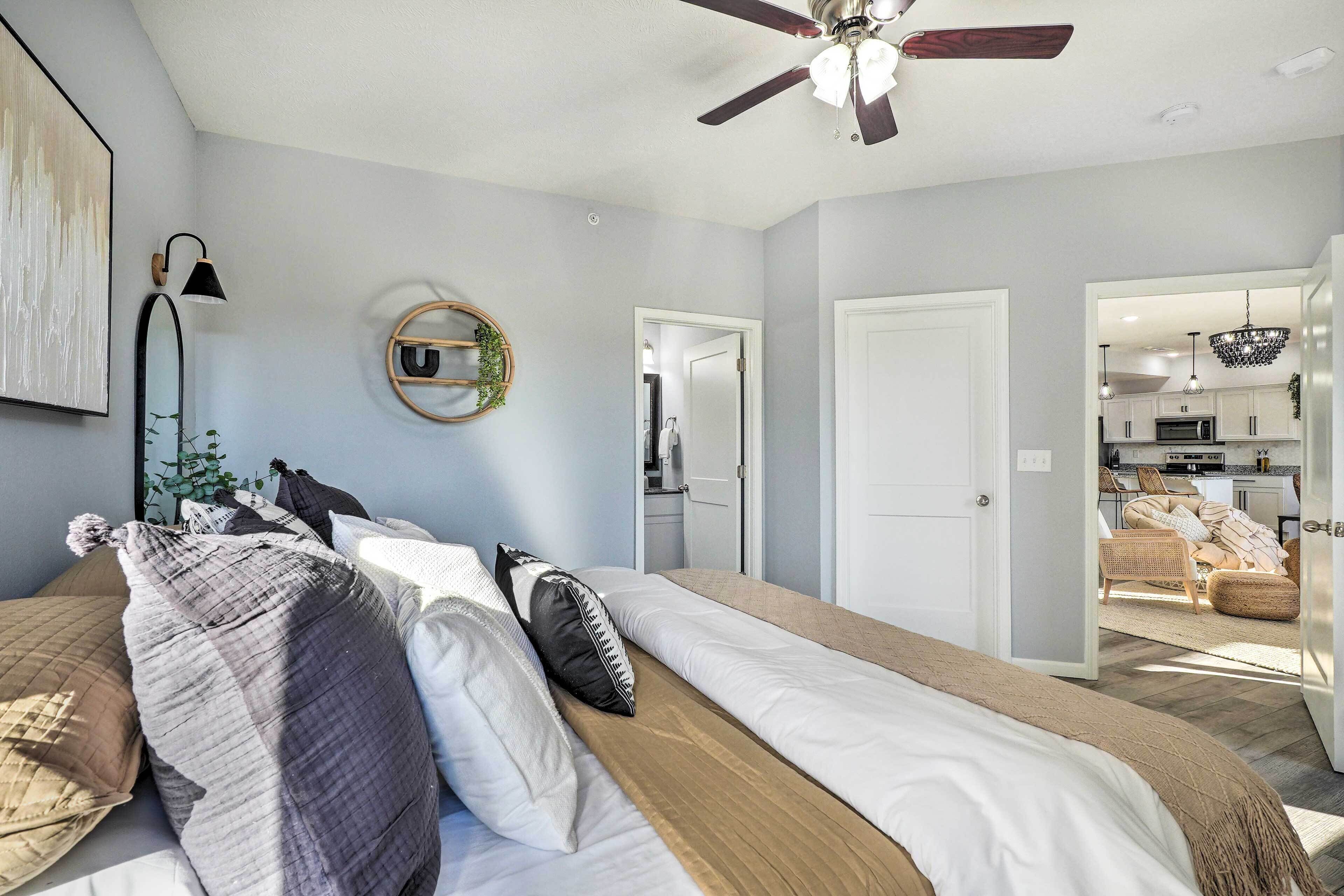 Een slaapkamer met een bed, een plafondventilator, een spiegel en uitzicht op de keuken.