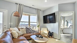 A modern living room with a leather sofa, a coffee table, and a TV mounted on the wall. - Reeds Spring Condo ~ 3 Mi to Silver Dollar City! (Branson West)