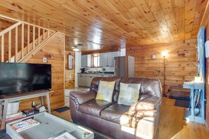 A wooden cabin interior with a leather sofa, a television, and a kitchen area.