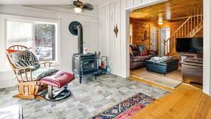 A cozy living room with a fireplace, a comfortable seating area, and a staircase leading to another room. - Center Ossipee Cabin w/ Game Room & Fire Pit! (Center Ossipee)
