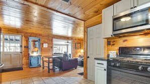 A wooden interior with a kitchen area including a stove, oven, microwave, and seating area with a table and chairs. - Center Ossipee Cabin w/ Game Room & Fire Pit! (Center Ossipee)