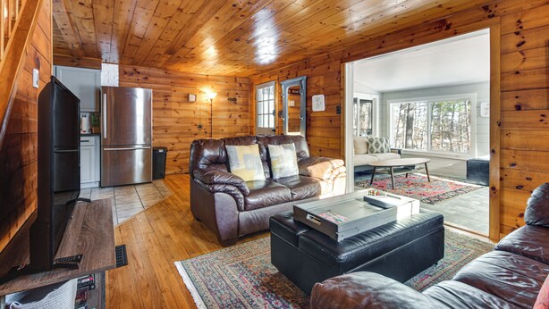 A cozy cabin interior with a wooden ceiling, a leather sofa, a dining table, and a kitchen area. - Center Ossipee Cabin w/ Game Room & Fire Pit! (Center Ossipee)