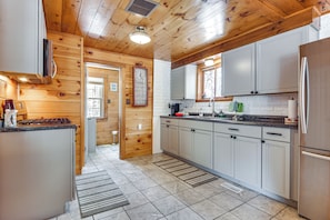 A modern kitchen with wooden walls, white cabinets, a stainless steel refrigerator, and a built-in oven.