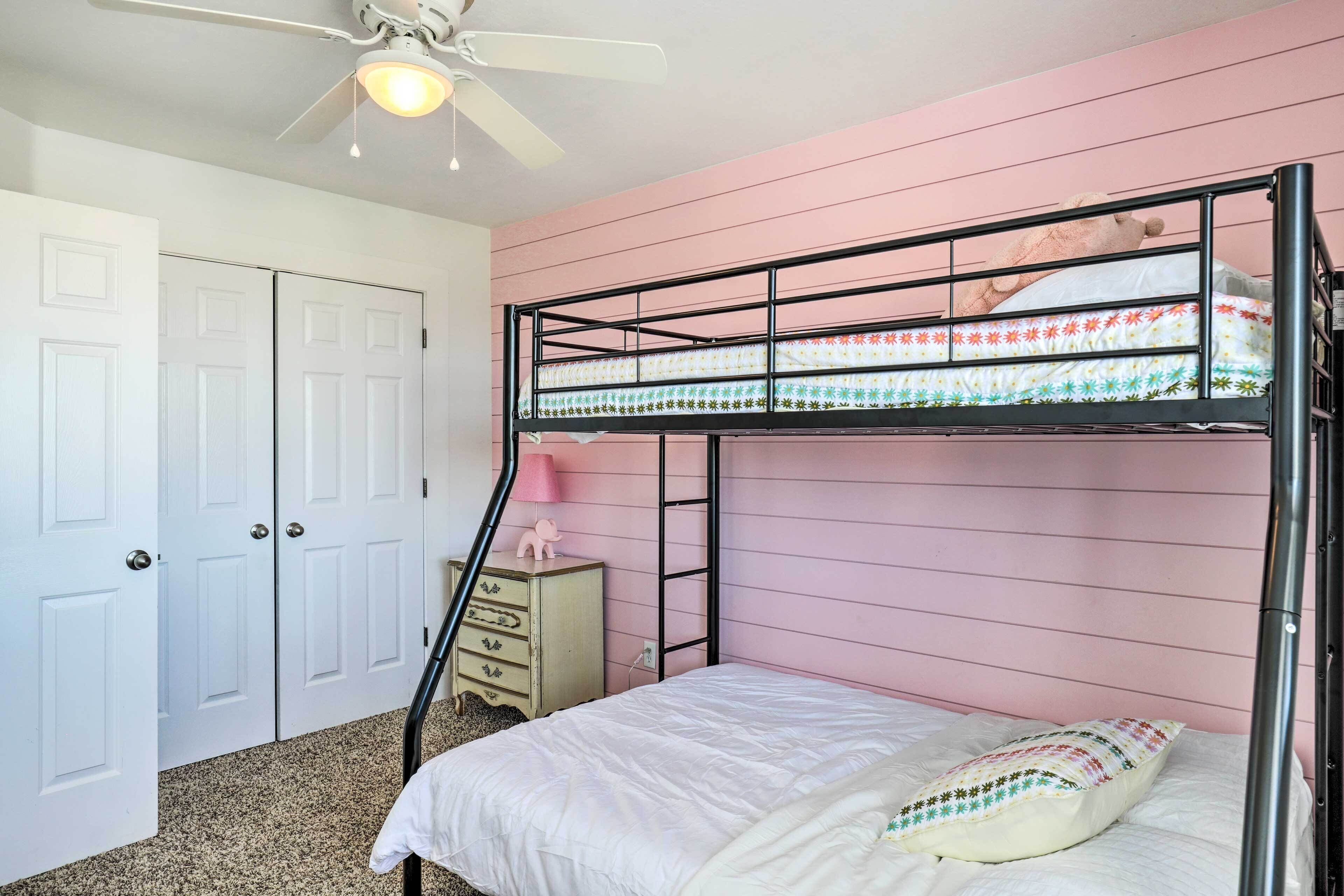 A bunk bed room with a ceiling fan, a dresser, and a door.