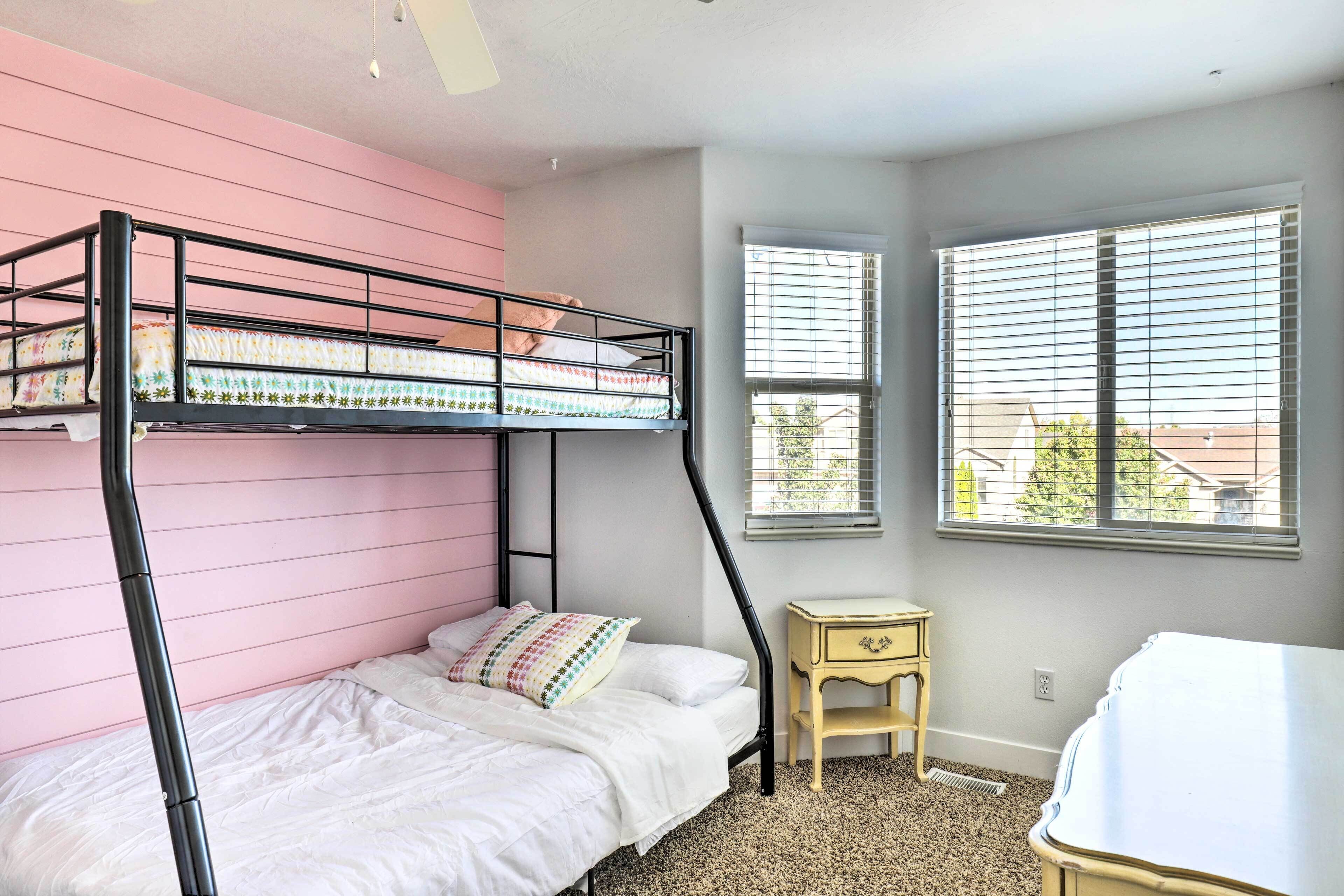 Una cama litera con una pared rosa, una mesita de noche de madera y una ventana con persianas.