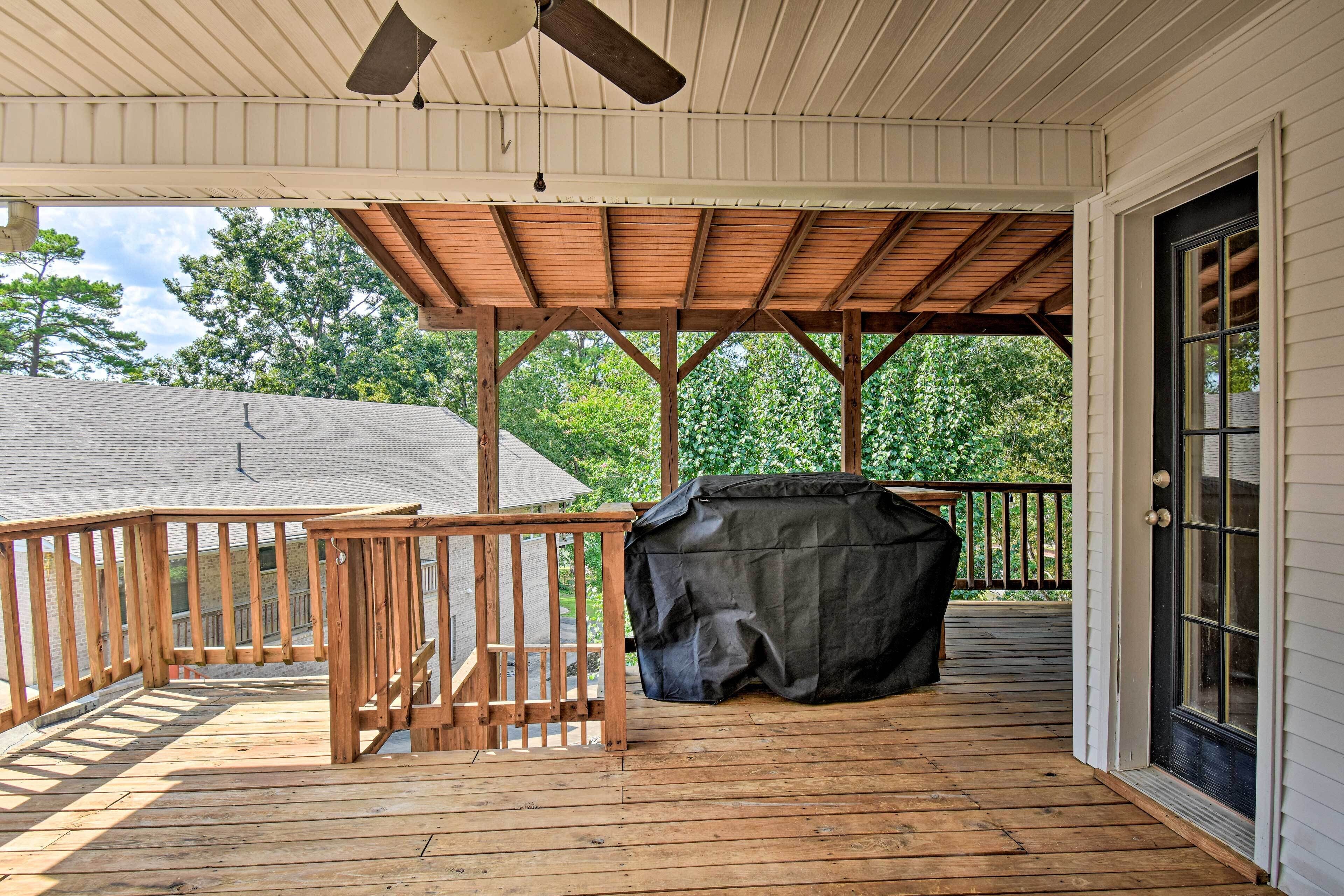 A covered wooden deck with a ceiling fan, a barbecue grill, and a view of a house in the background.