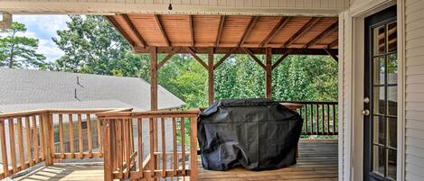 A covered wooden deck with a ceiling fan, a barbecue grill, and a view of a house in the background.