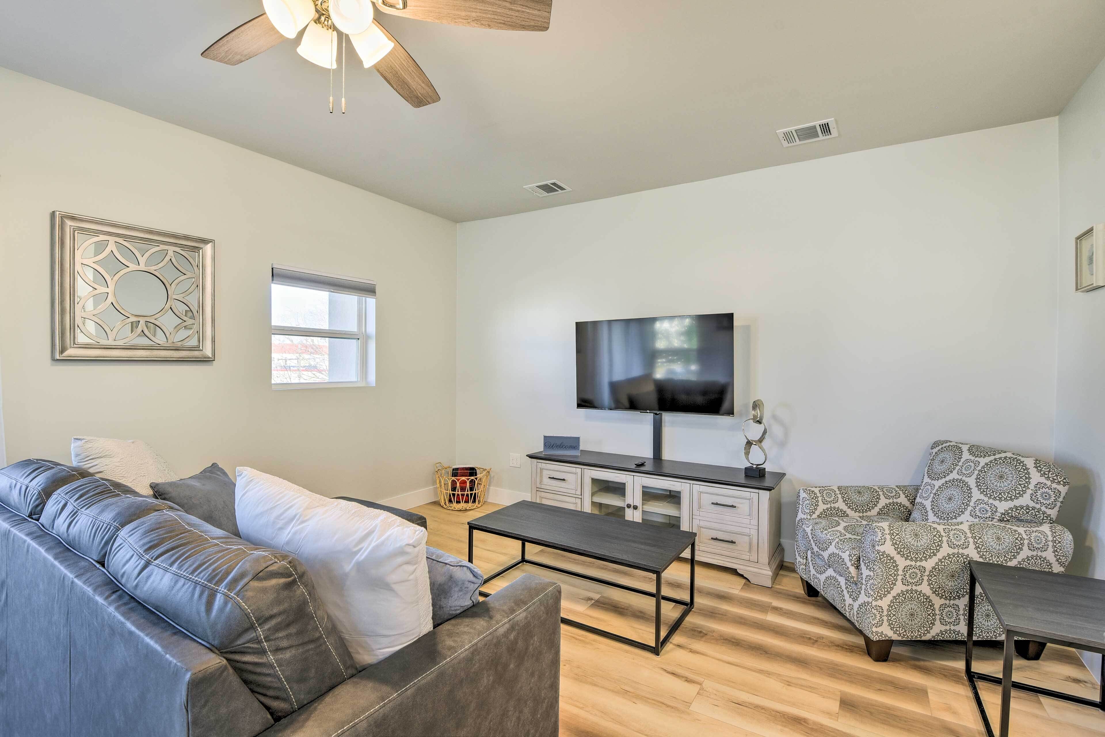 A modern living room with a grey sofa, a patterned armchair, a coffee table, a TV, and a ceiling fan.