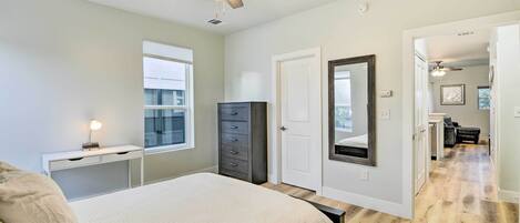 A bedroom with a bed, a dresser, a ceiling fan, a window, and a door leading to another room.