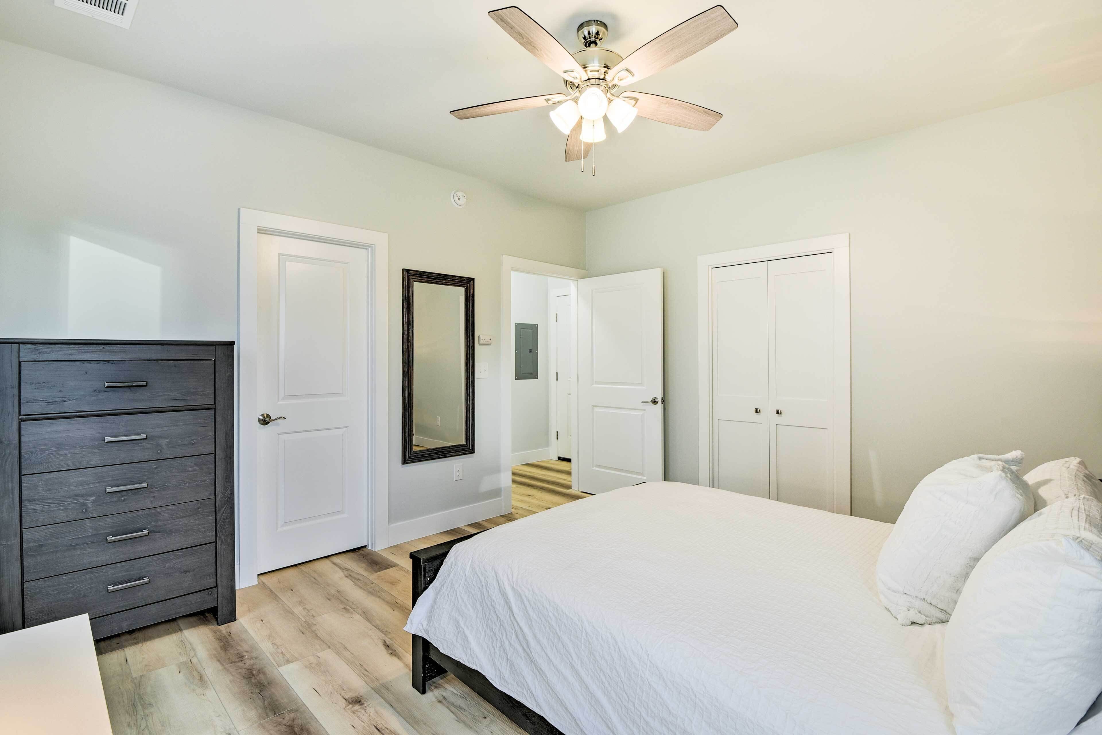 A bedroom with a bed, a dresser, a ceiling fan, and white doors.