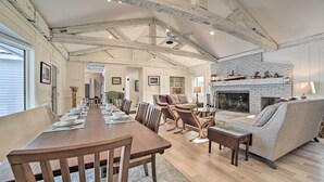 A spacious living area with a long wooden dining table, comfortable seating, a fireplace, and exposed wooden beams on the ceiling. - Waterfront Suttons Bay: Wine Trail, Pickleball Ct (Suttons Bay)