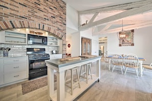 A kitchen with a brick wall, modern appliances, and a dining area with white chairs and a wooden table. - Waterfront Suttons Bay: Wine Trail, Pickleball (Suttons Bay)