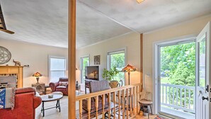 Un salon spacieux avec un canapé rouge, une table basse en bois et une cheminée. Il y a un balcon avec une balustrade et une porte donnant sur l’extérieur.