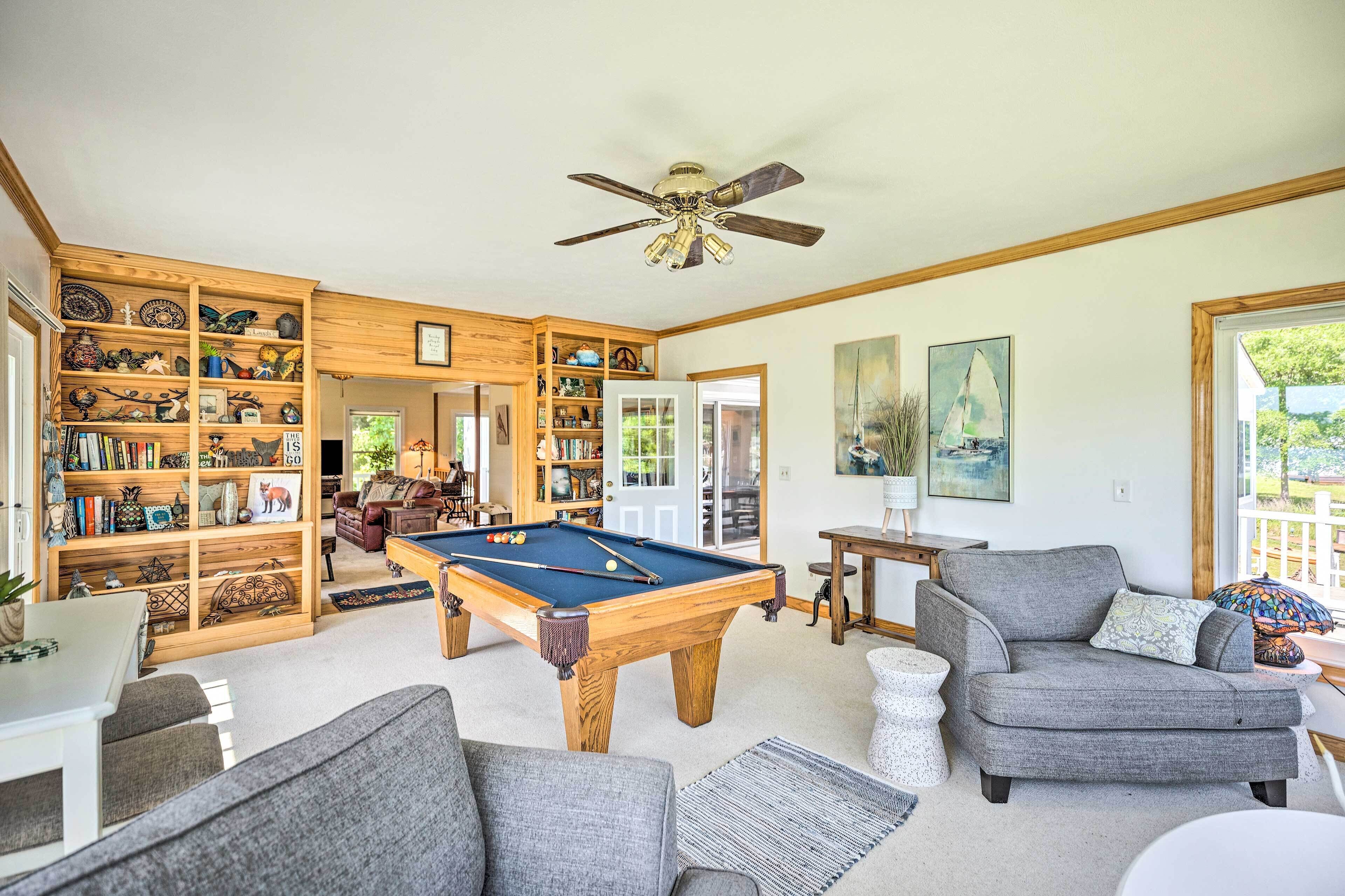 Un salon spacieux avec une table de billard, des sièges confortables et une bibliothèque en bois remplie d’objets décoratifs.