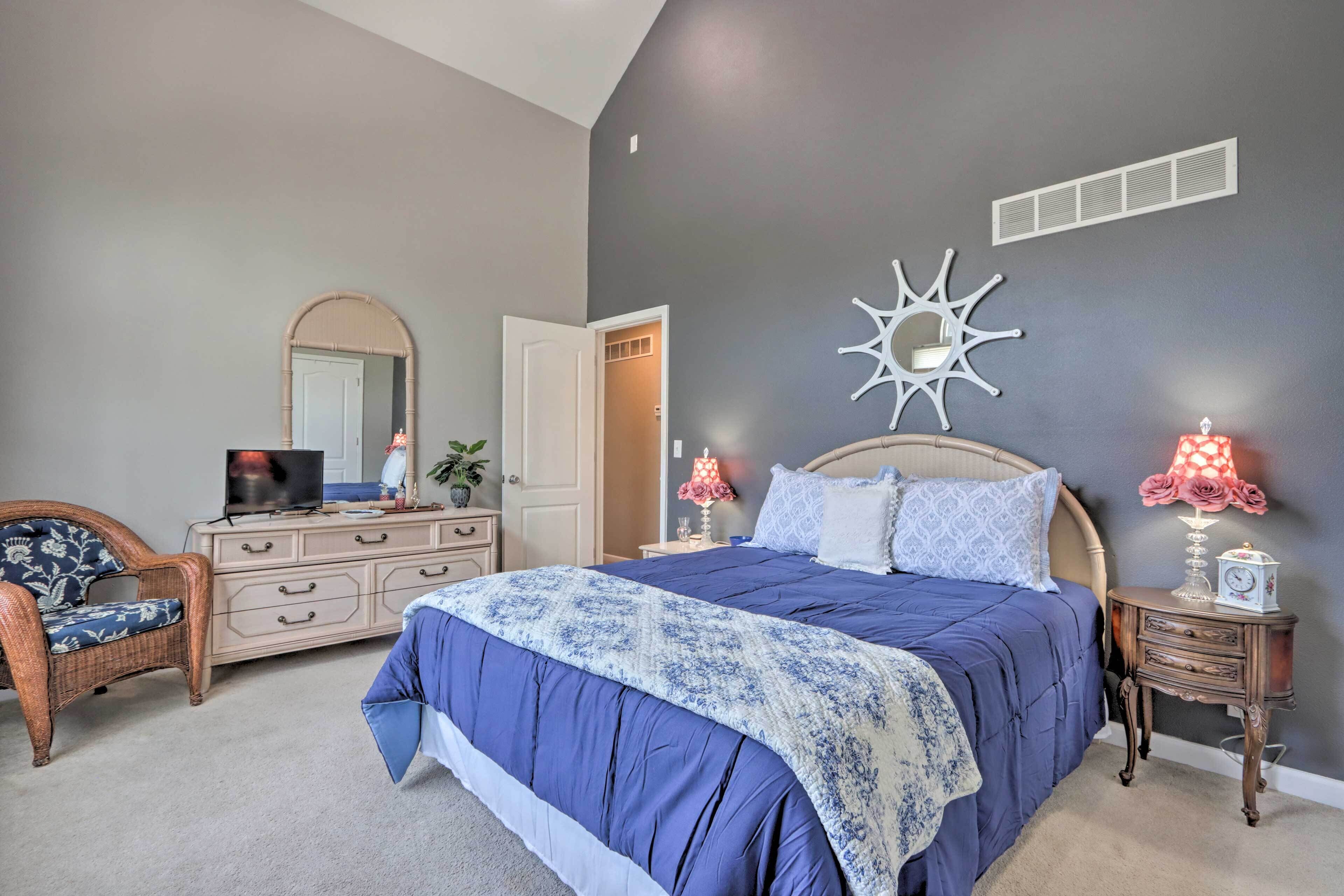 A bedroom with a large bed, a dresser, a chair, a mirror, and a wall decoration.