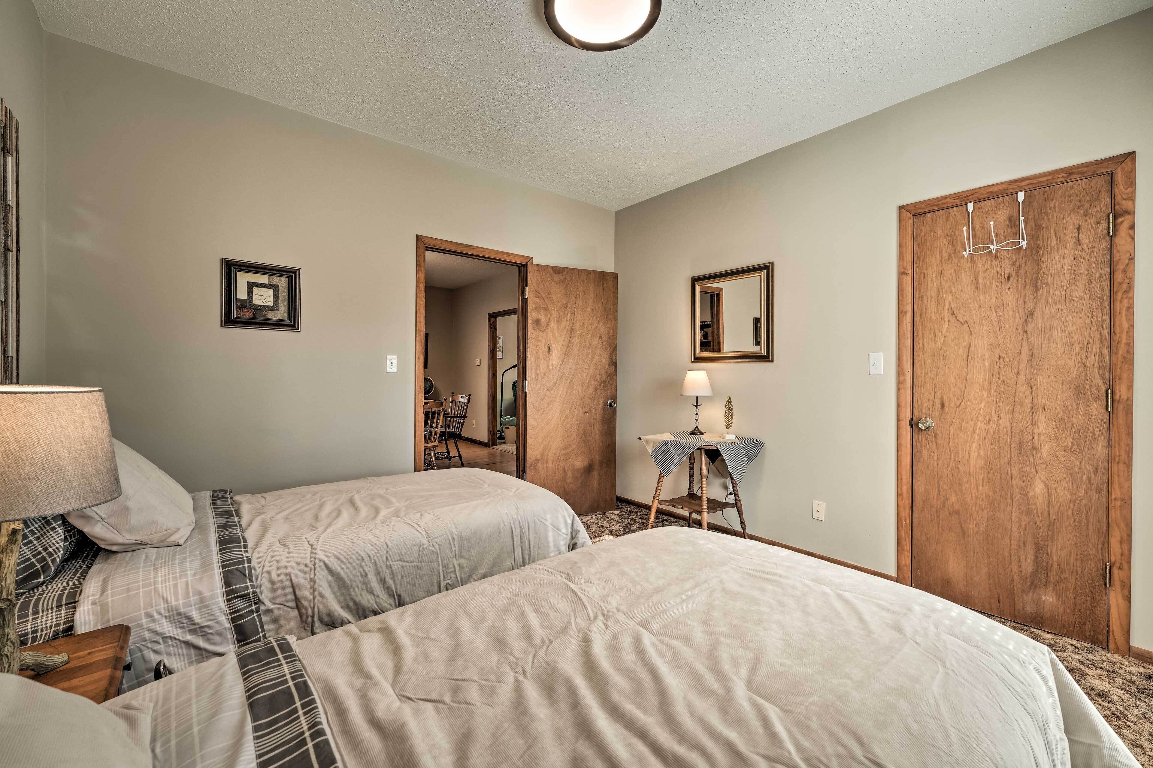 Habitación de hotel con dos camas, un armario de madera, un espejo, una mesita de noche con una lámpara y un cuadro en la pared.