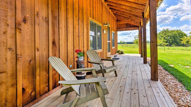 Una terraza de madera con sillas Adirondack, una planta en maceta y vistas a un paisaje verde.