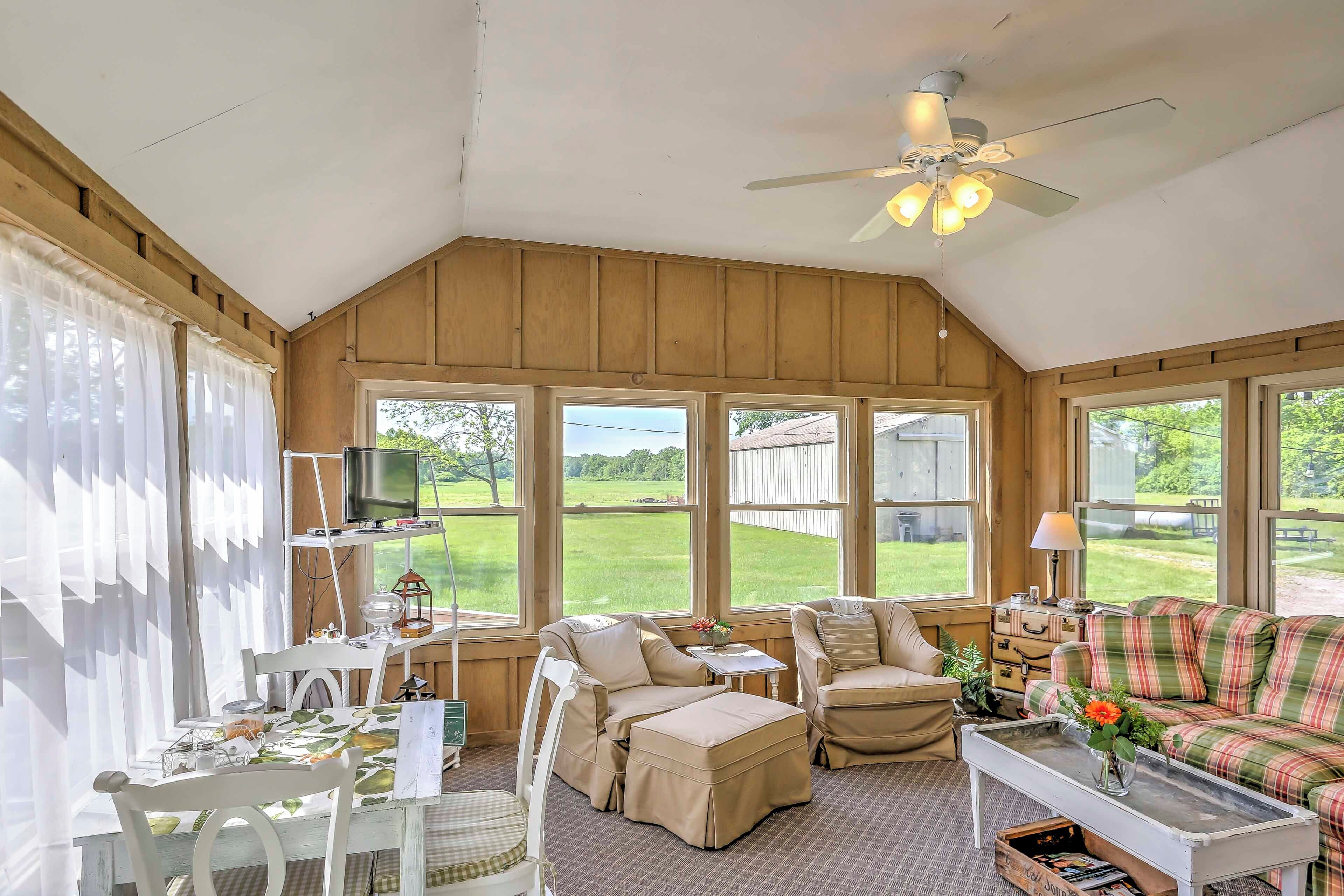A cozy room with a large window, a ceiling fan, and a plaid sofa.