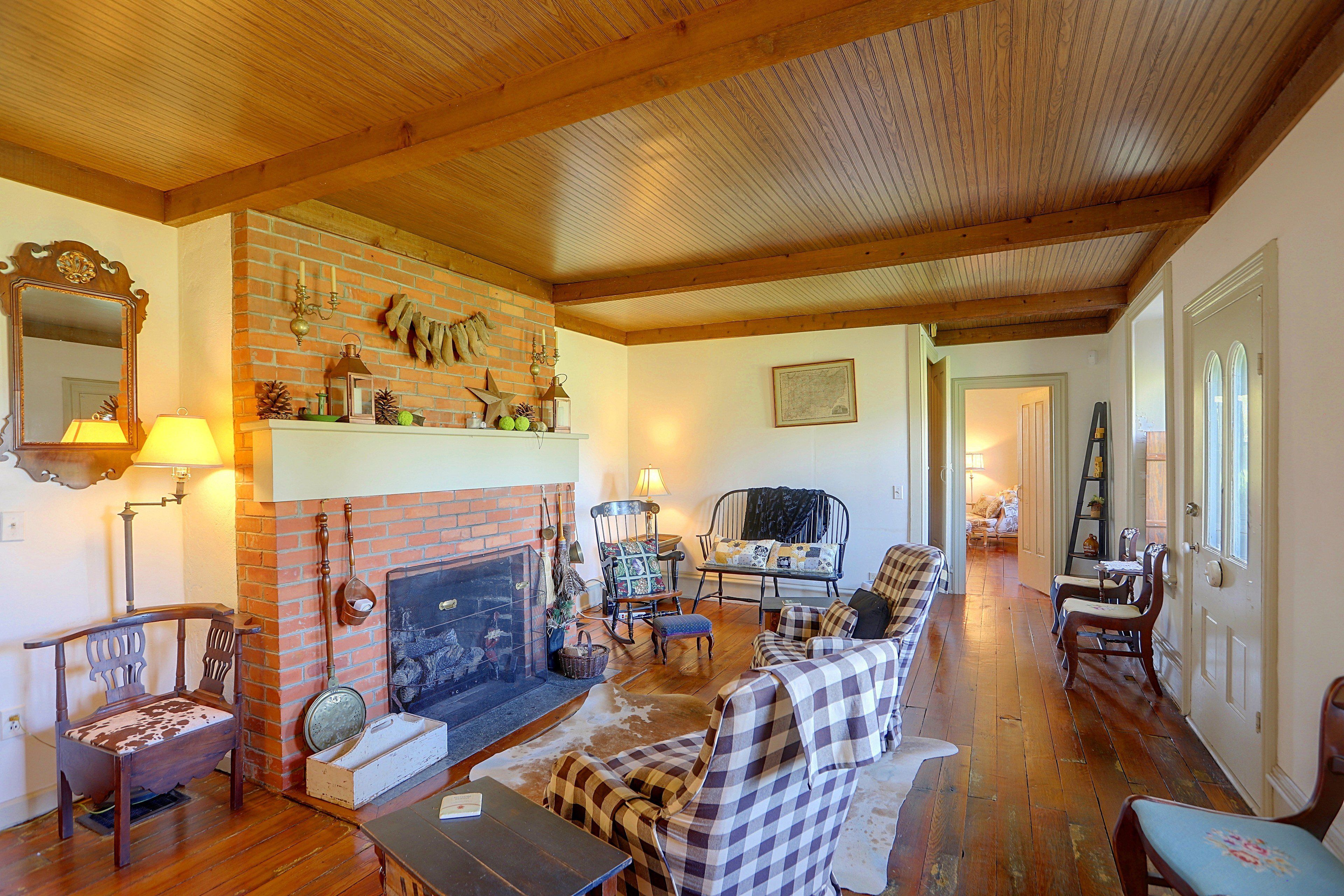 A cozy living room with a fireplace, wooden floors, and a mix of seating including a sofa and chairs.