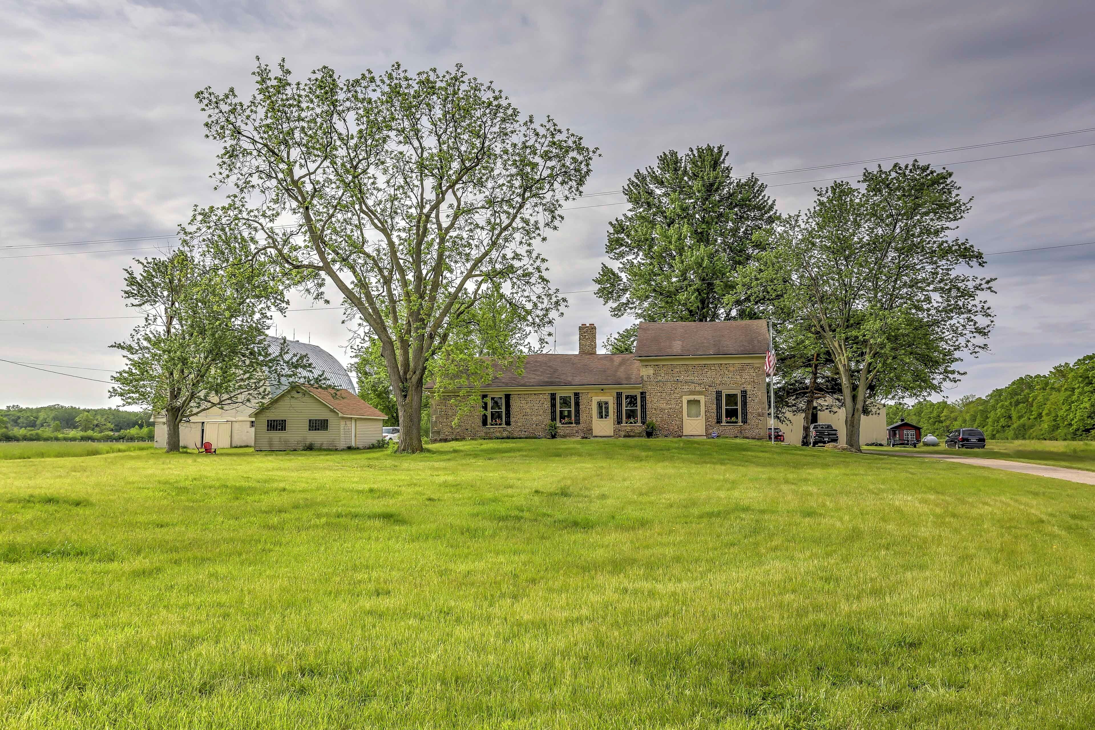 A two-story house with a brick exterior, surrounded by a large grassy field and trees.