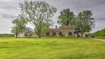 A two-story house with a brick exterior, surrounded by a large grassy field and trees.