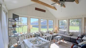 A sunlit room with a dining table, chairs, a sofa, and a ceiling fan.