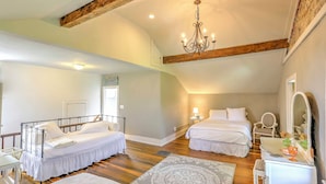 Une chambre spacieuse avec deux lits, un lustre, une coiffeuse avec un miroir et une poutre en bois au plafond.