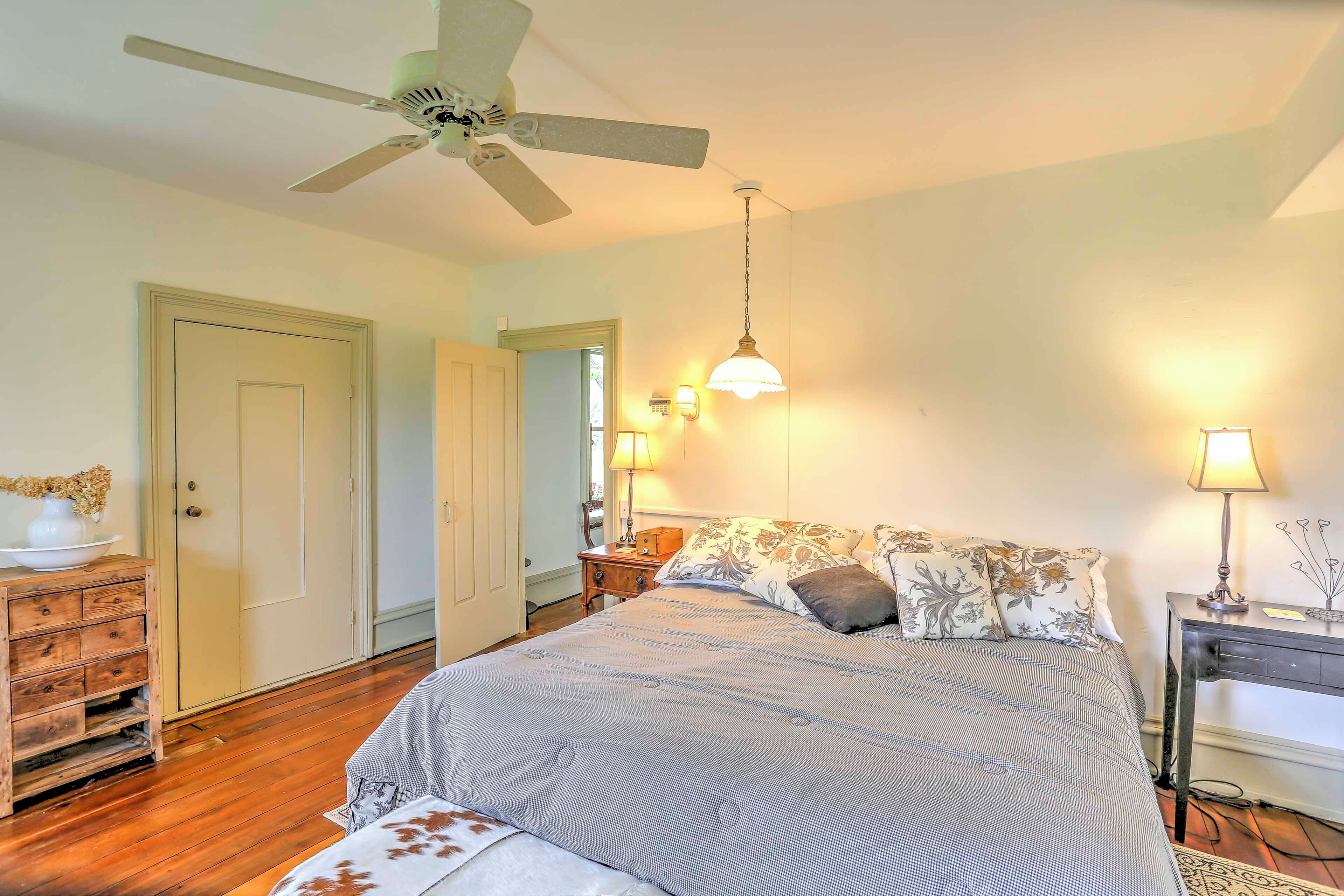 A bedroom with a bed, a ceiling fan, bedside lamps, a dresser, and a door.