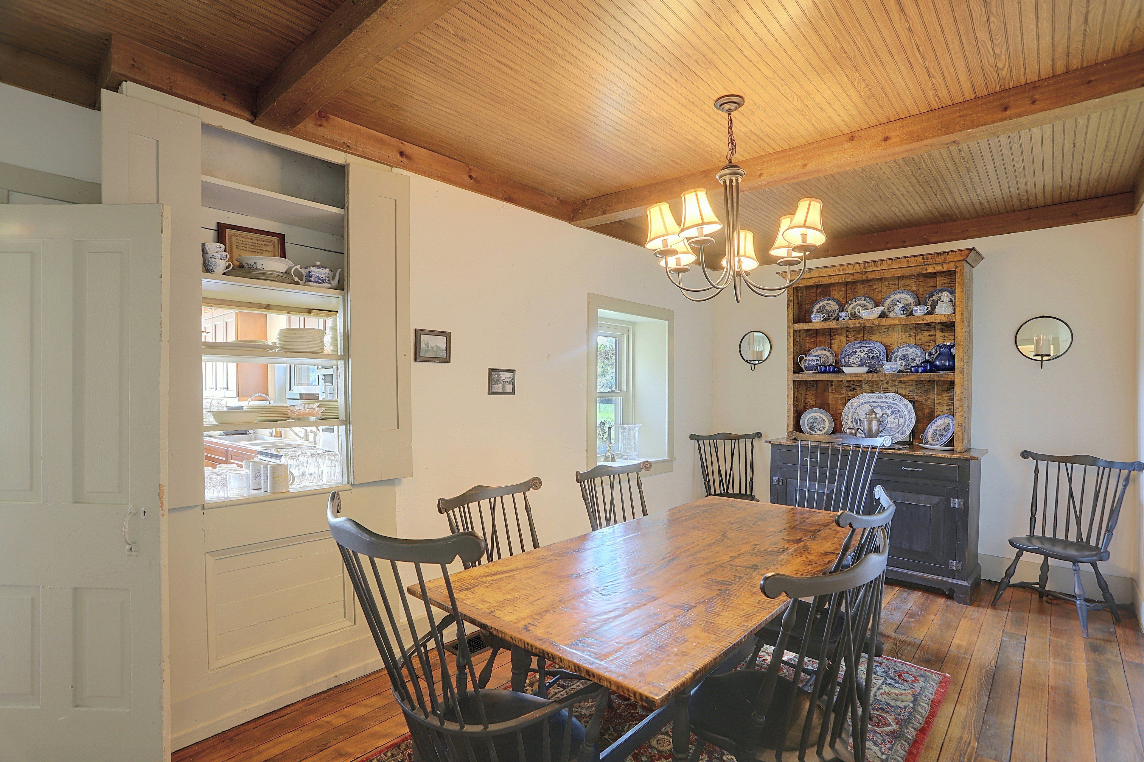 A dining area with a wooden table and chairs, a chandelier, and a shelf with dishes.