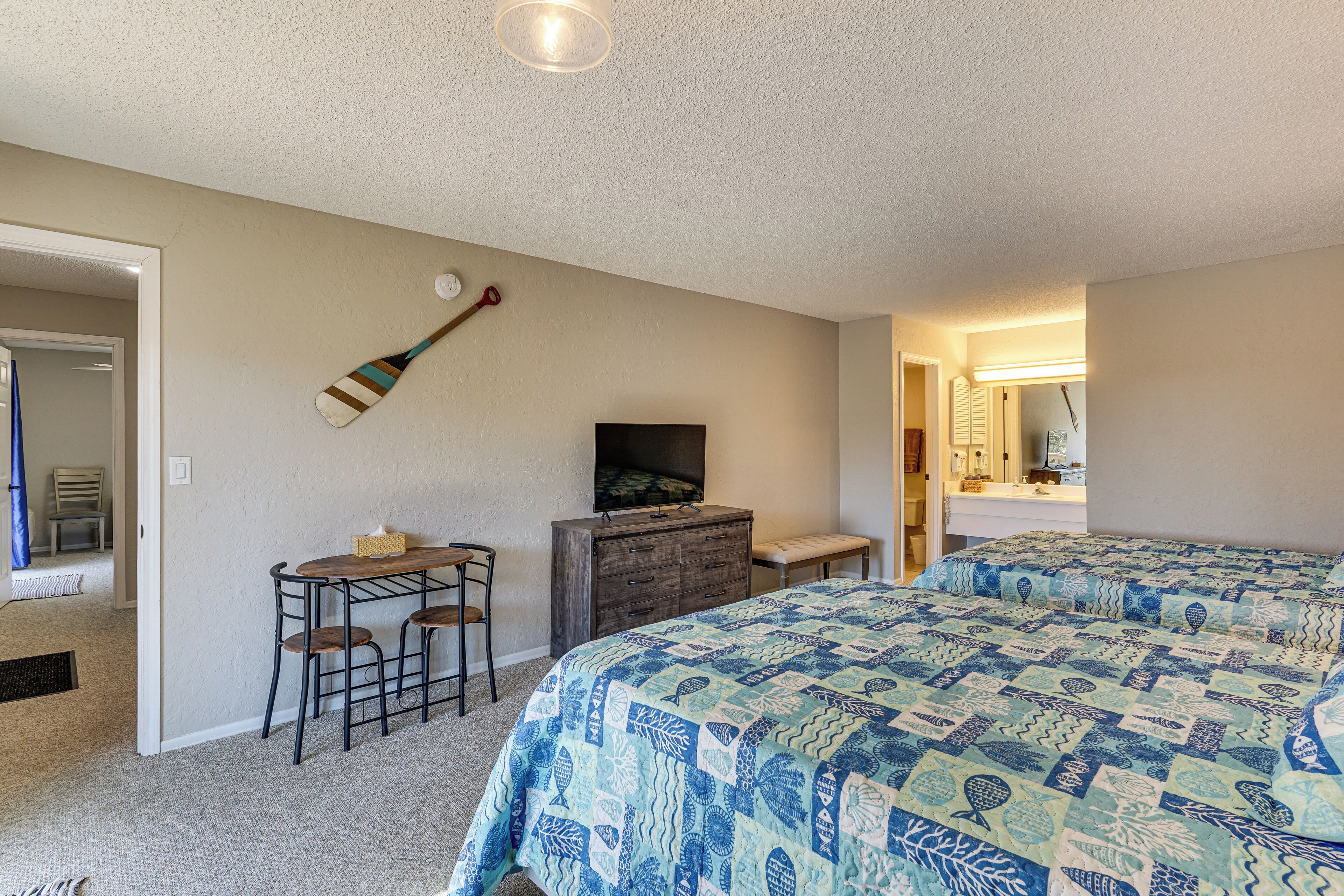 A bedroom with two beds, a desk with a chair, a dresser, and a television.