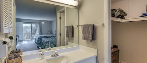 Un baño con un espejo grande, lavamanos blanco y un perchero para toallas.