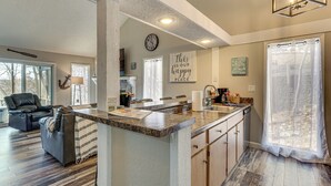 A spacious living area with a large window, a comfortable seating area, and a kitchen with a central island. - Walk to Lake: Osage Beach Home w/ Grill! (Osage Beach)