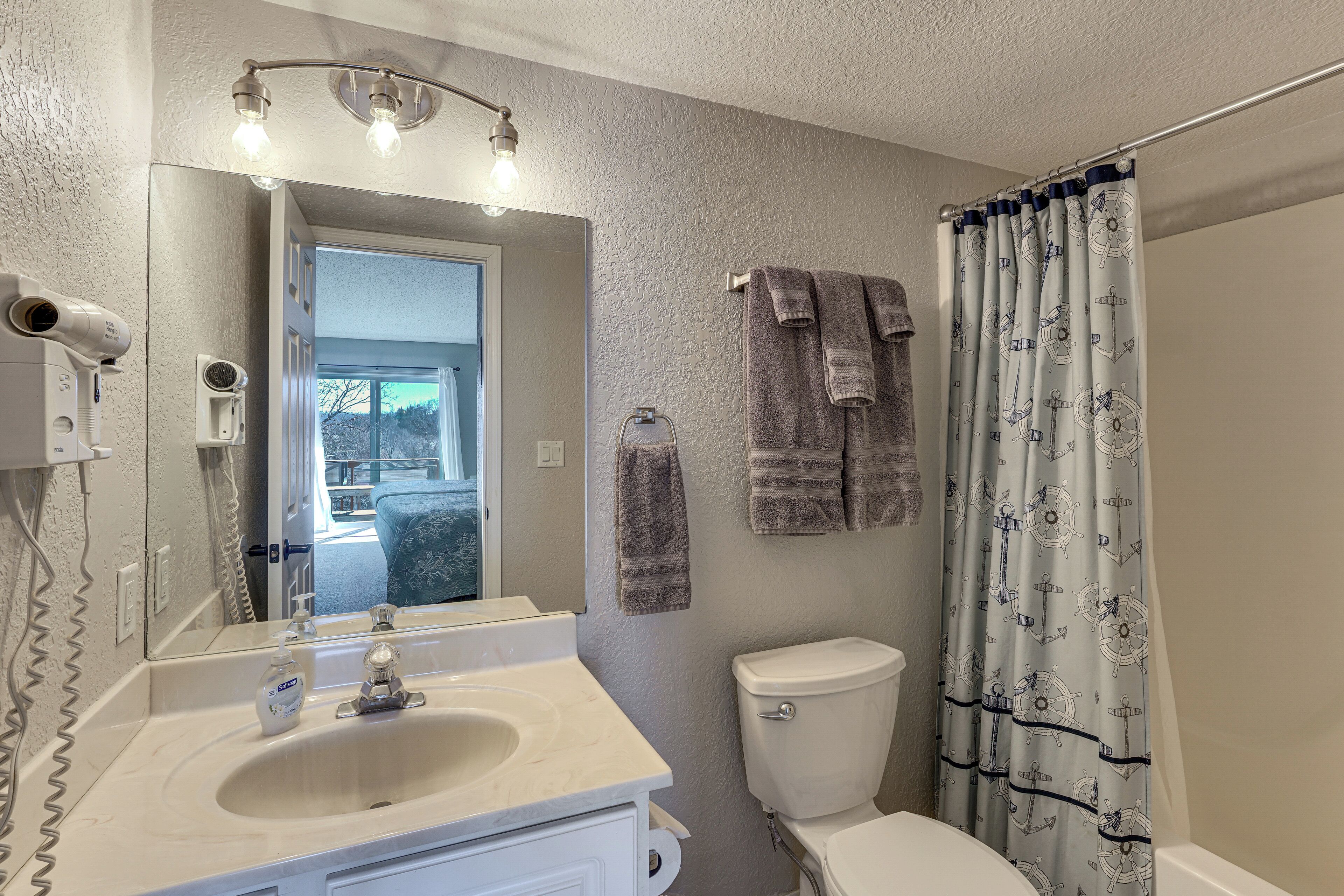 A bathroom with a sink, mirror, and toilet. There are towels hanging on the wall and a shower curtain with a nautical pattern.